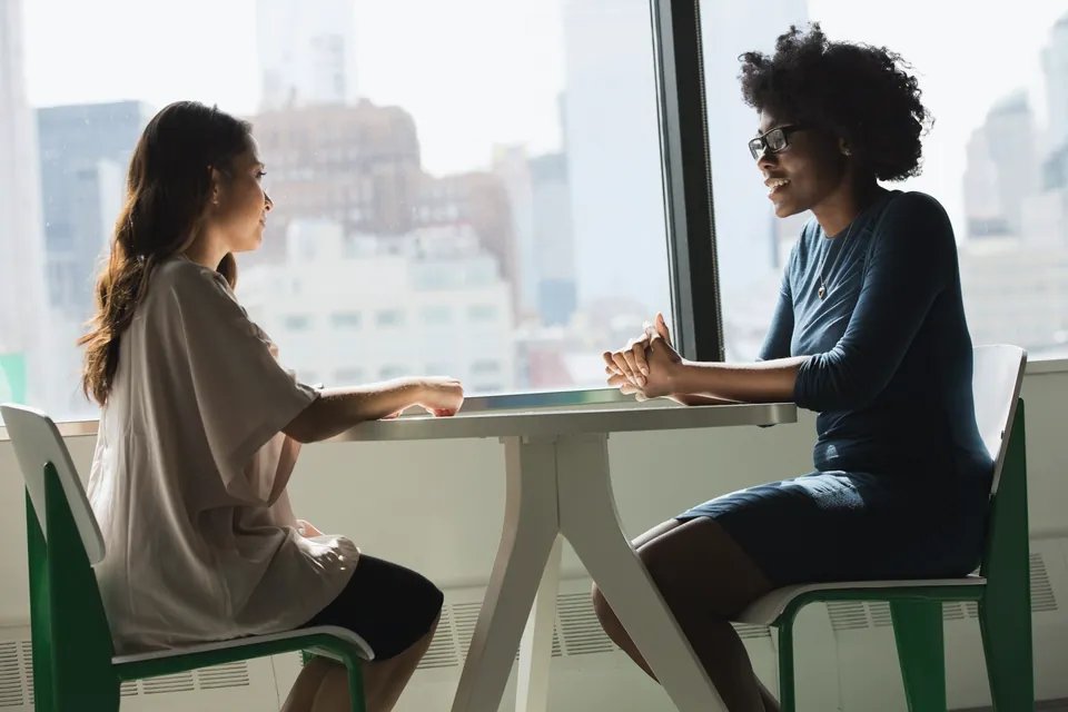Two people in conversation at a table by a window
